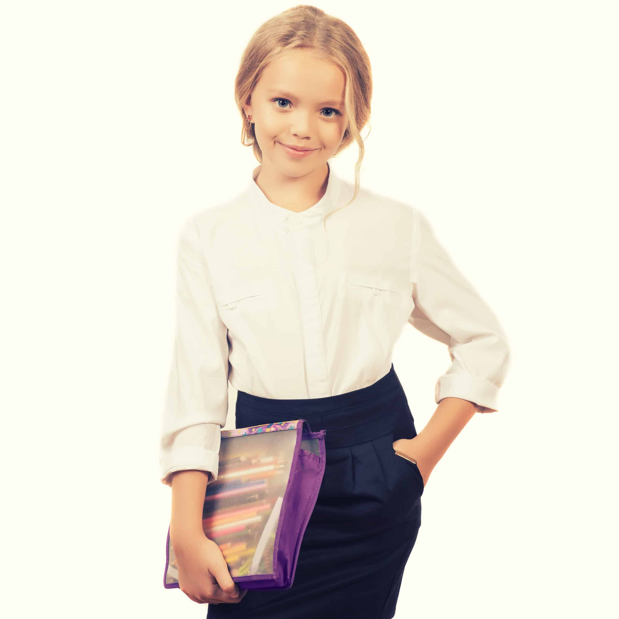 School girl isolated on white. Child in uniform with school supplies smiling at camera. Caucasian kid with pencils case.